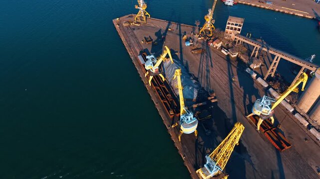 Aerial perspective of industrial dock with loading cranes. Top down view of port terminal machinery and cargo storage area.
