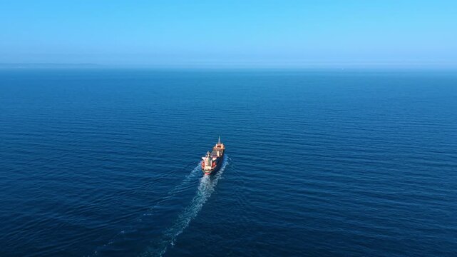 Top down aerial shot of ship in ocean. Perspective of a cargo vessel sailing in deep blue sea.