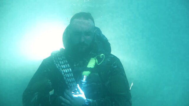 Man in military equipment opens his eyes underwater, close-up. Portrait