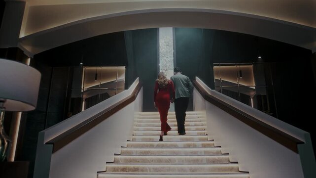 Smartly dressed man and woman walk together up the stairs to the terrace of an upscale restaurant during a romantic date