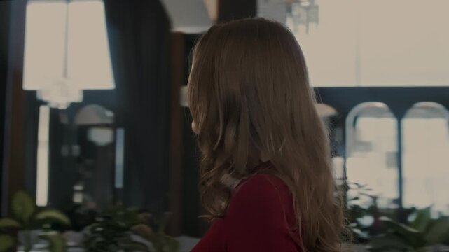 Gorgeous girl in an evening red dress and beautiful makeup looks around in the interior of an expensive restaurant