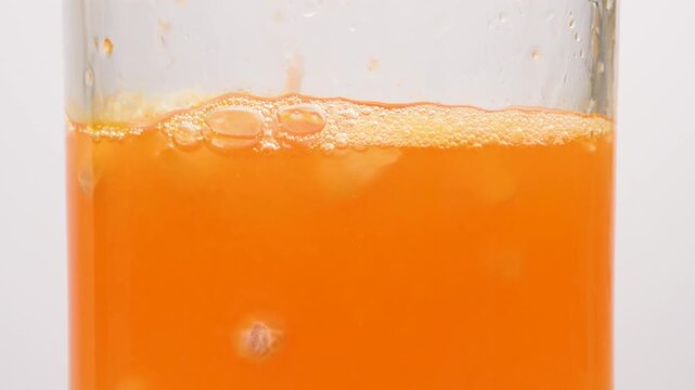 Extreme macro close-up of fresh orange juice with bubbles and pulp being poured into a glass on a white background. Vibrant healthy drink.