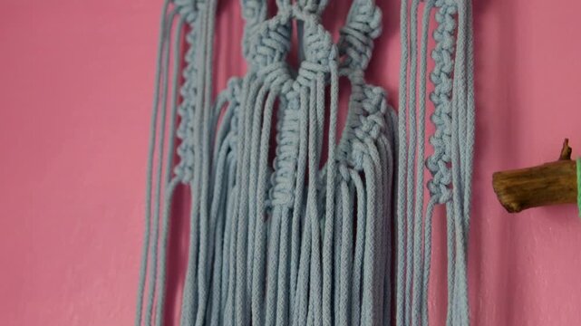Handmade macrame wall decor on pink rural house wall with traditional woven patterns creating cozy boho atmosphere and authentic countryside interior style