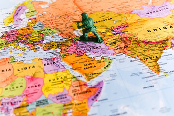 Naklejka premium single green plastic toy soldier in a kneeling, aiming pose is positioned on a detailed colorful political map centered on the Middle East and Central Asia