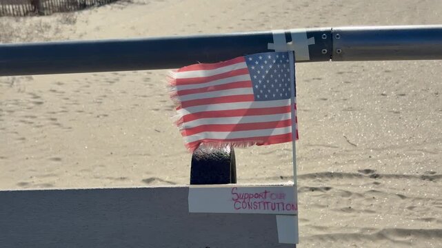 Small American flag on a windy day attached to a rail at the beach.