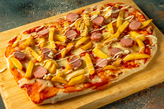 ast food pizza with french fries, sausage slices, melted cheese and mayonnaise served on wooden board