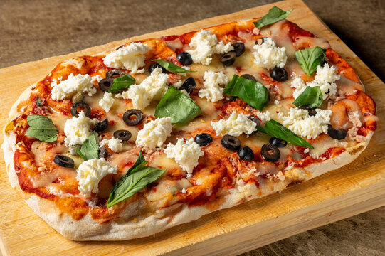 Italian pinsa bufalina with tomato sauce, buffalo mozzarella, black olives, capers and basil served on wooden board