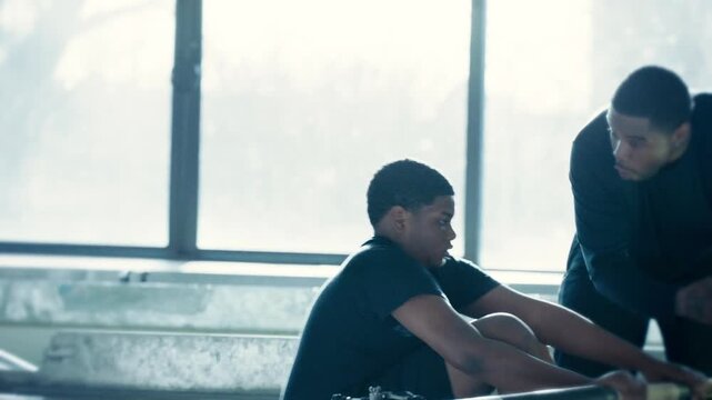 Dedicated African American male trainer teaching a child how to use an indoor rowing machine at the gym