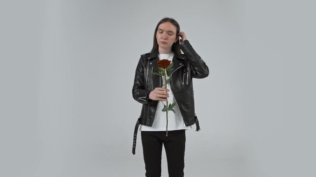 Young attractive guy with long hair standing on a white background with a rose flower in his hands 