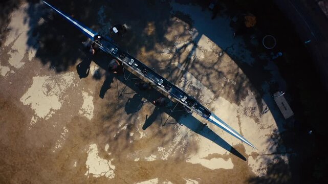 Top down aerial view of a team of rowers carrying their boat to the dock before practice