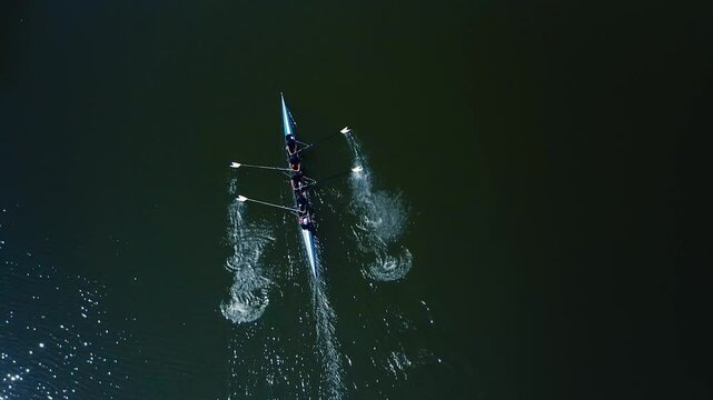 Team of four athletes rowing a shell in perfect synchronization on a river during training