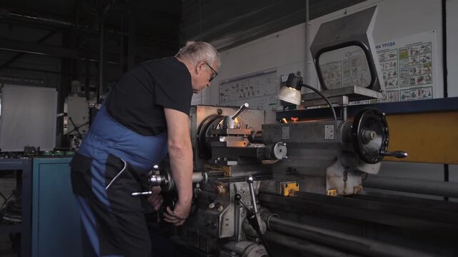 Elderly man in a work uniform works on a huge lathe