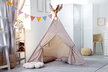 Stylish toy wigwam, furniture, pillows and decor in light playroom. Interior design © New Africa