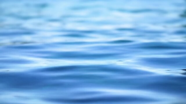 Close-up video of serene, clear blue water surface with gentle ripples, shimmering light, and a natural blue gradient. Soft daylight tracking video; meditative abstract background