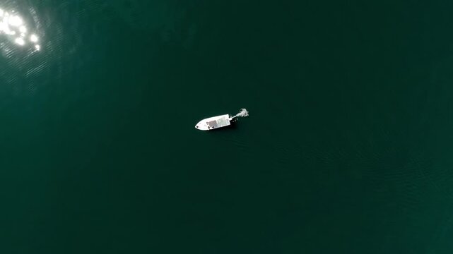 Small tourist boat adrift in vast azure ocean, captured in a minimalist composition with endless water surrounding it, sunlight shimmering across the surface and creating soft reflections and tranquil