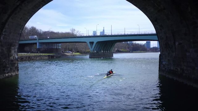 Young athletes training in a rowing shell seen through a bridge arch on the Schuylkill River