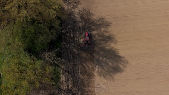 Agricultural field under cultivation: A red tractor plows a field, preparing the soil for planting, highlighting the ongoing cycle of agriculture and the connection to the earth.
