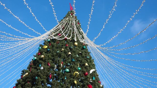 Bright lights twinkle against a clear blue sky as a majestic Christmas tree towers proudly. Colorful ornaments adorn its branches, creating a festive atmosphere that captures the magic of winter