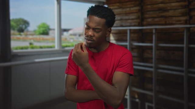 Man with hand on chin in building interior near window and railing wearing red shirt with furrowed brow; doubt.