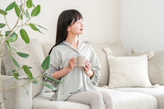 An Asian woman relaxes at home in the morning, drinking tea or hot water from a mug (a way to promote warmth).