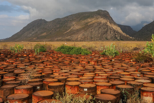 Rusty oil drums polluting nature under a cloudy sky