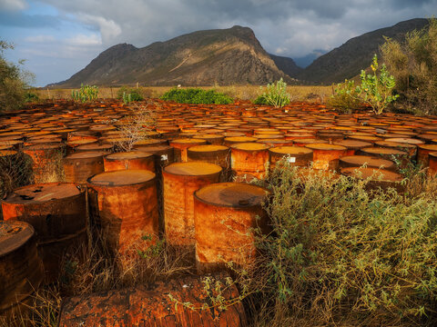 Rusty oil drums polluting nature under a cloudy sky