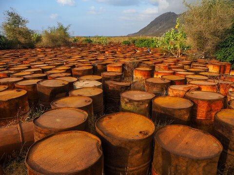 Rusty oil drums polluting nature under a cloudy sky