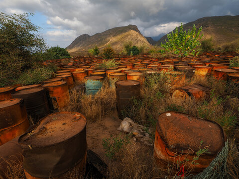 Rusty oil drums polluting nature under a cloudy sky