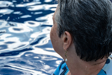 Profile portrait of a happy senior woman with short gray hair smiling in a swimming pool, active aging and healthy retirement lifestyle concept, summer vacation at a luxury resort © Sergio Palacio