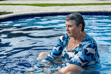 Profile portrait of a happy senior woman with short gray hair smiling in a swimming pool, active aging and healthy retirement lifestyle concept, summer vacation at a luxury resort © Sergio Palacio