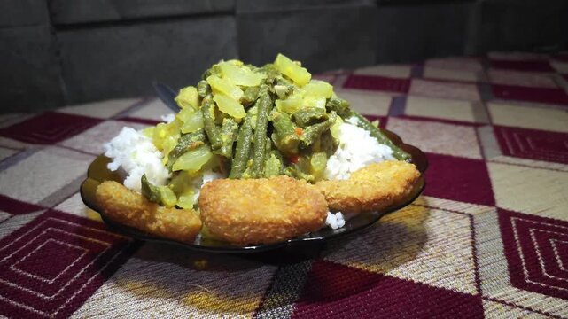 Plate of white rice with stir fried green beans and chicken nuggets served on a glass plate over a patterned tablecloth