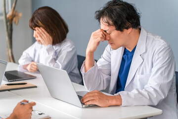 Obraz premium A male doctor holding his head due to overwork and fatigue (poor health, lack of sleep, doctor shortage, stress)