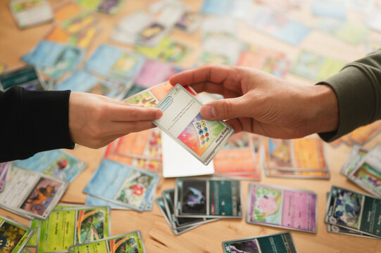 Chicago, IL/USA - March 26, 2026: Close up overhead photo of two anonymous people's hands trading two Pokemon cards over table covered in Pokemon card collection