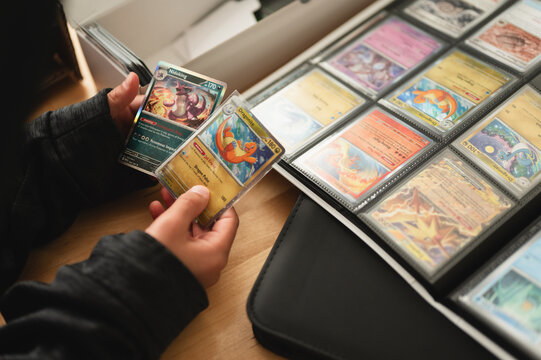 Chicago, IL/USA - March 26, 2026: Close up overhead photo of anonymous child's hand holding two Pokemon cards next to binder with organized Pokemon card collection from 151 set