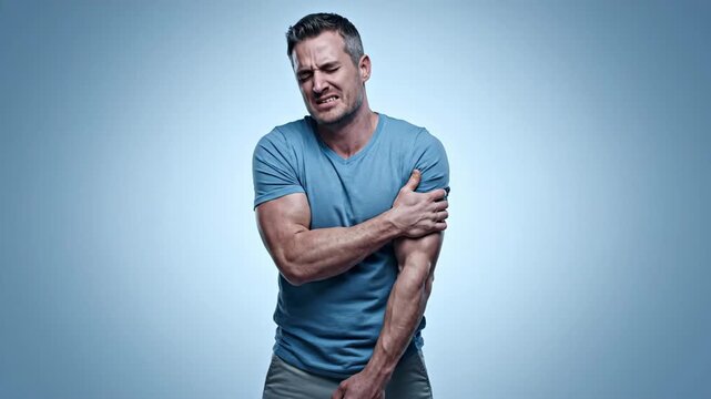 A man in a blue t-shirt clutches his arm in pain, grimacing. The blue gradient background and studio lighting emphasize his discomfort.