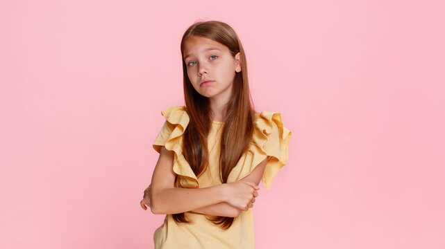 Young child girl imitates a serious expression and uses a watching you gesture, pointing two fingers from eyes toward the camera with a focused look. School kid on pink background, playful expressive.