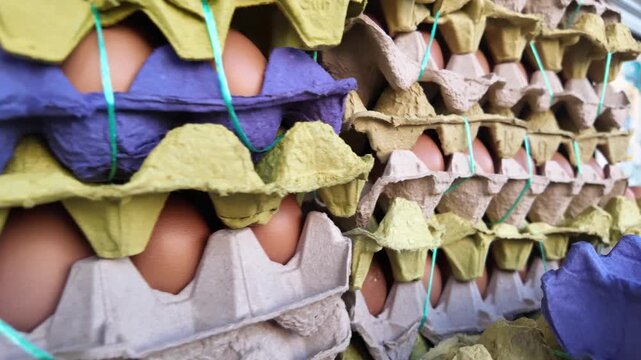 Close up of fresh raw chicken eggs stacked in colorful paper trays at local market.