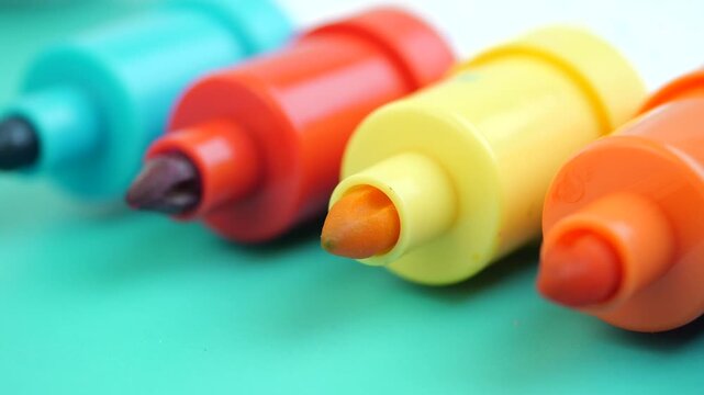 Colored markers arranged in a line on a turquoise background, stationery tools in close-up motion shot.