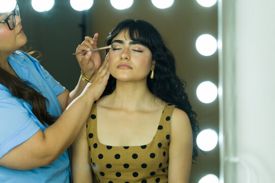 Latin model backstage, getting her makeup done by a professional, preparing for a photoshoot or event