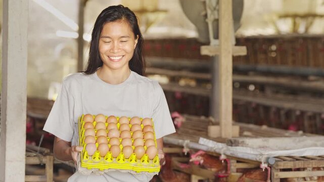 Young filipino adult egg farmer on poultry farm with chickens or hens in battery cages in background, smiling portrait, looking at camera