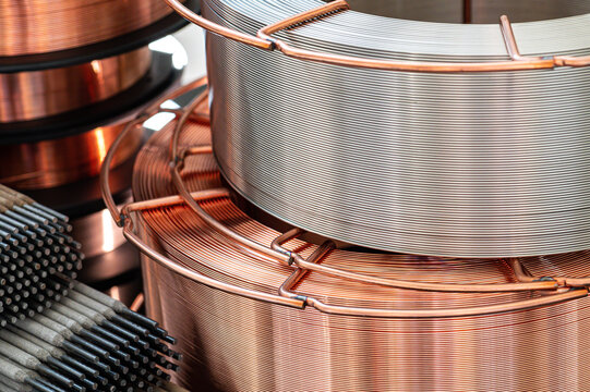 Horizontal view of stacked welding wire spools and electrodes. Industrial still life of copper wire coils and bundles of metal arc welding rods on black background