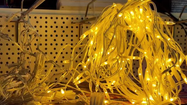 Yellow LED String Lights Piled On Pegboard Shelf, Shopper Inspecting Tangled Warm Strands, Bright Amber Glow Spilling Across Metal Hooks, Store Display Showcasing Varied Color
