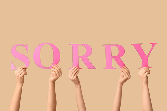 Female hands with word SORRY on beige background