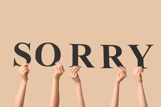 Female hands with word SORRY on beige background