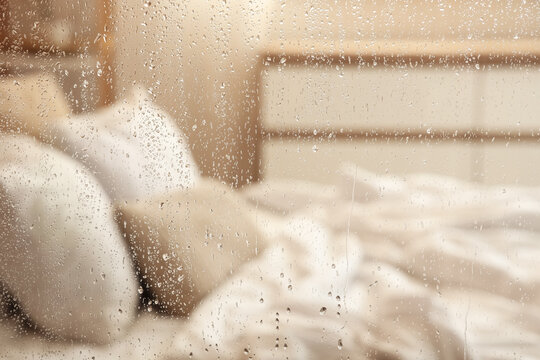 Water droplets on glass against blurred bed in room, closeup
