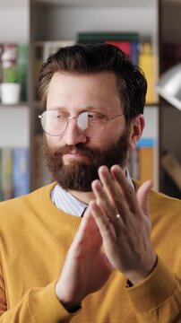 Man sarcastic applause. Vertical video of gloomy skeptical bearded man in glasses in office or apartment room reluctantly claps his palms to create fake applause