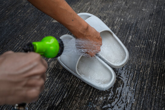 people washing rubber slippers with water hose and plastic brush, cleaning on house yard, natural background