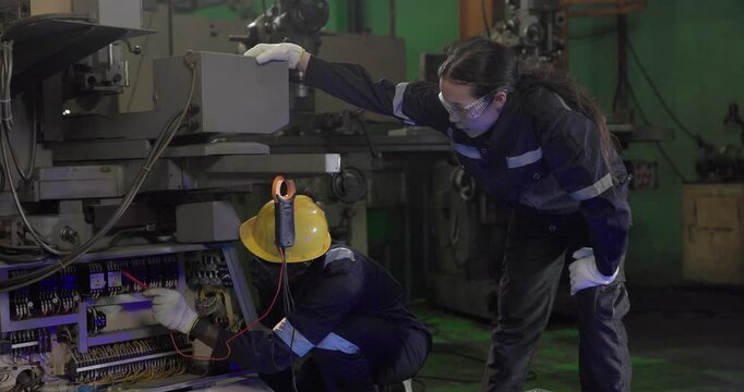 Factory technicians perform electrical inspection on an open control cabinet beside production machinery during maintenance in an industrial plant, showing diagnostics, repair, and safety.
