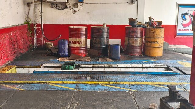 An empty car inspection and oil change pit inside a traditional automotive repair shop with rusted Lubrax oil barrels in the background