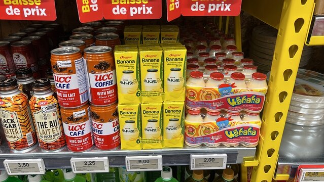 Colorful display of various beverage cans and cartons on supermarket shelf, featuring UCC coffee, banana juice, and Yagafa drink, showcasing vibrant product packaging